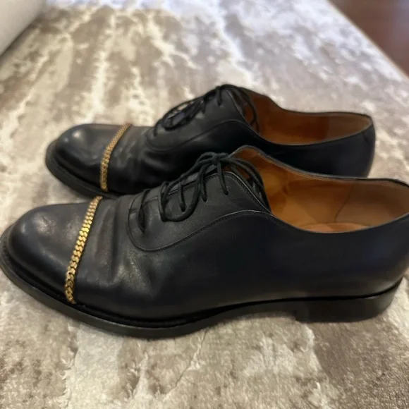 Gucci men’s black dress shoe with gold chain hardware.
